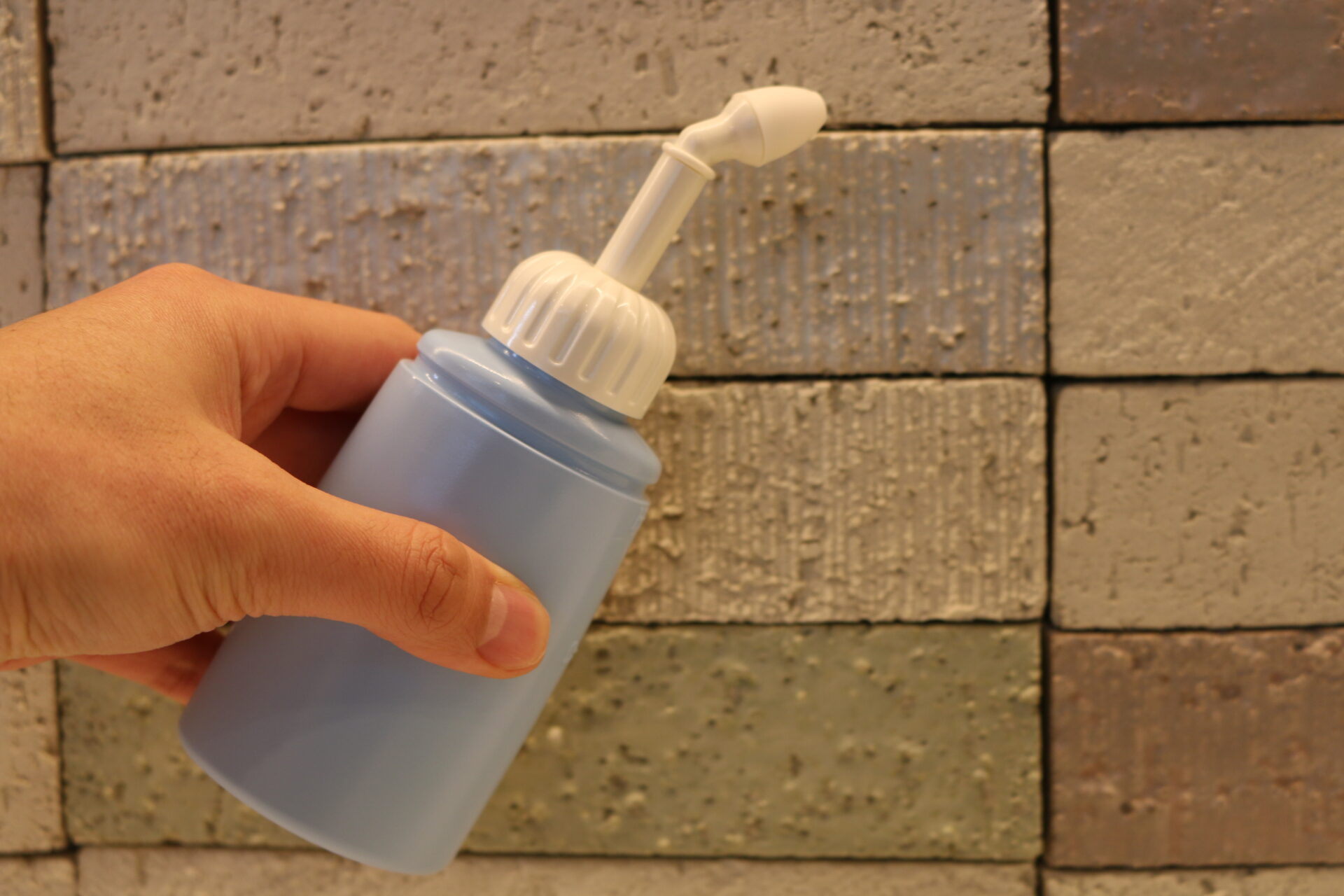 白い肌とグレーの T シャツを着た女性が、専用の器具を使って鼻を洗いながら首を傾げています。